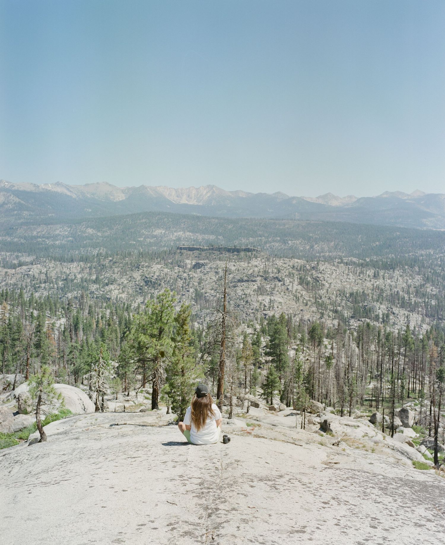 Panoramic mountain vista with snow patches and sparse evergreen trees stretching across a rocky landscape.
