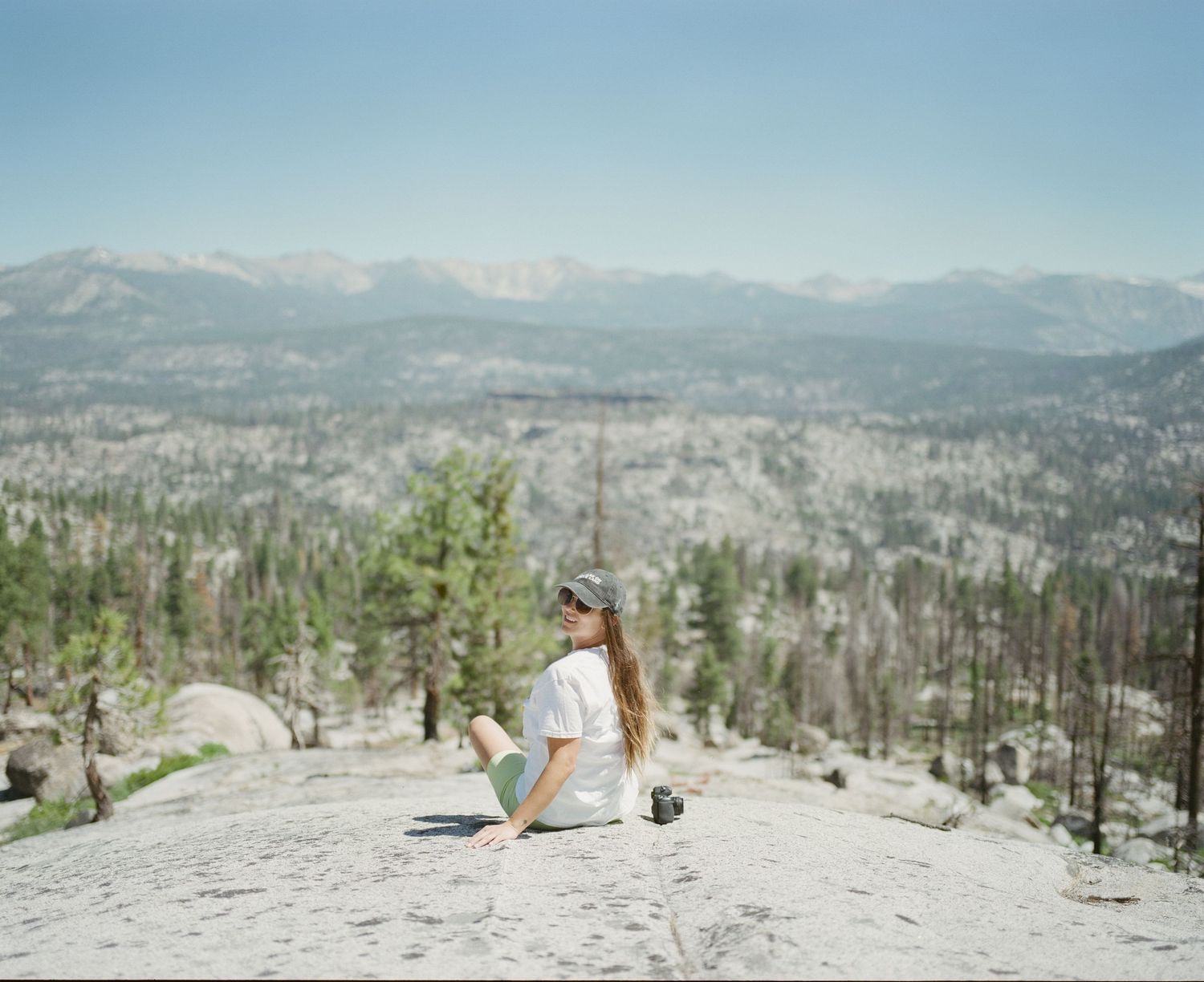Scenic mountain overlook with scattered pine trees and snow patches under clear blue skies.
