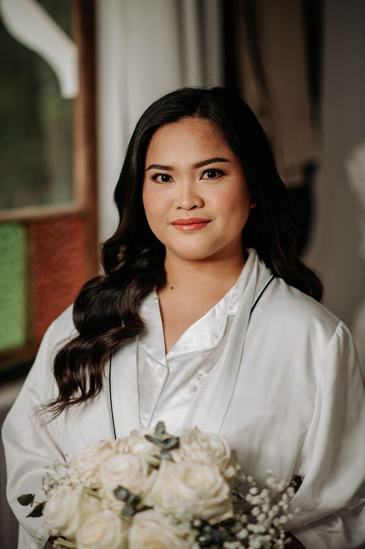 A person in a white silk robe holding a bouquet of white roses during wedding preparations.