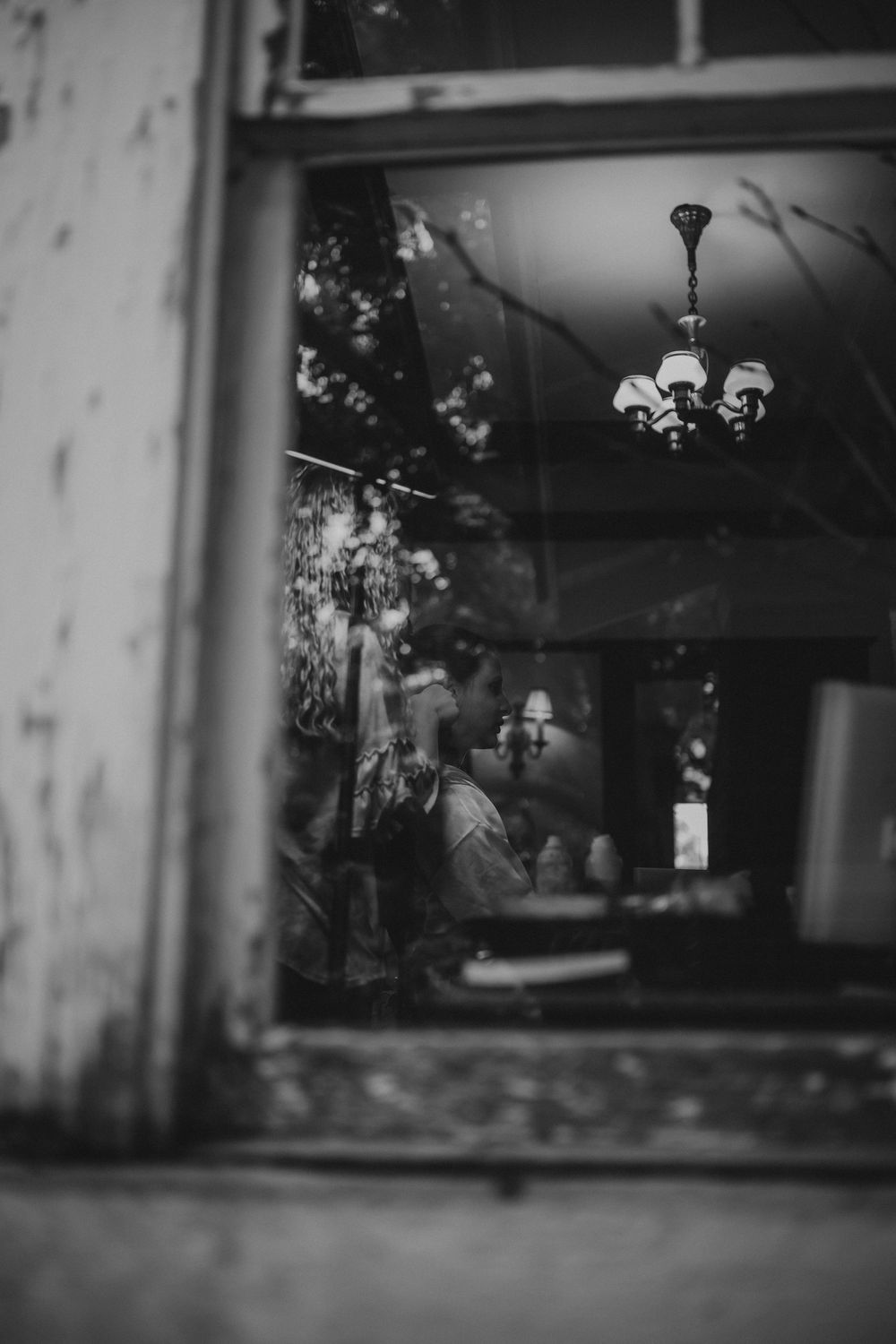 Black and white photo of a couple kissing inside a rustic venue, viewed through a weathered window.