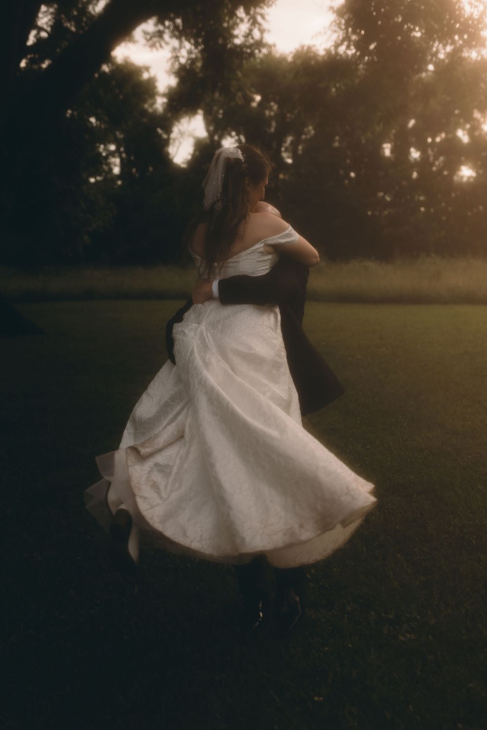 Bride and groom dancing outdoors at golden hour, her white gown swirling in a wooded setting.