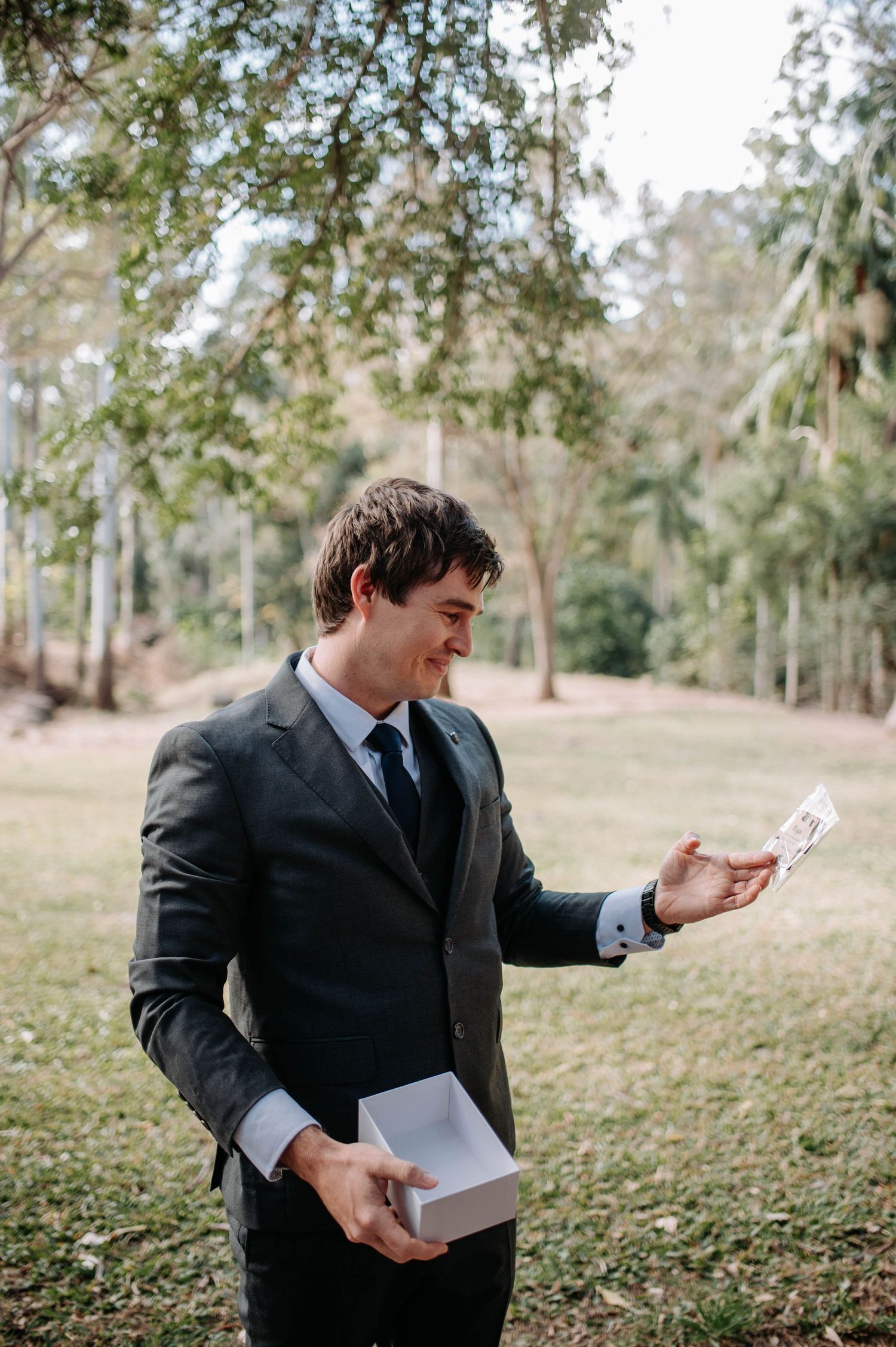 Person in a dark suit joyfully reads a letter while standing in a wooded outdoor setting.