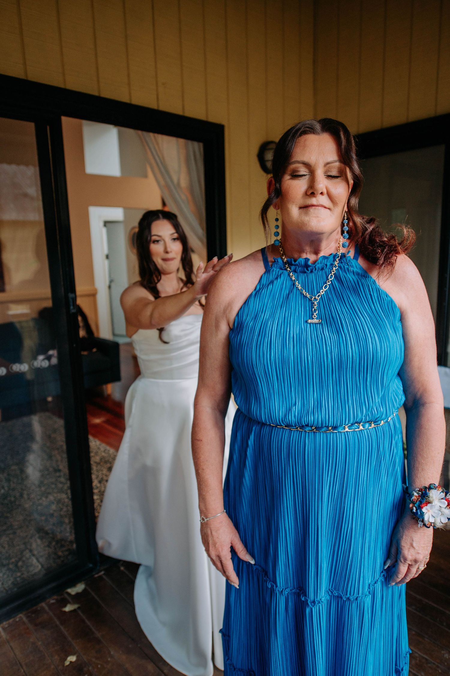 A person in a blue pleated dress stands while a wedding dress is visible in the background.
