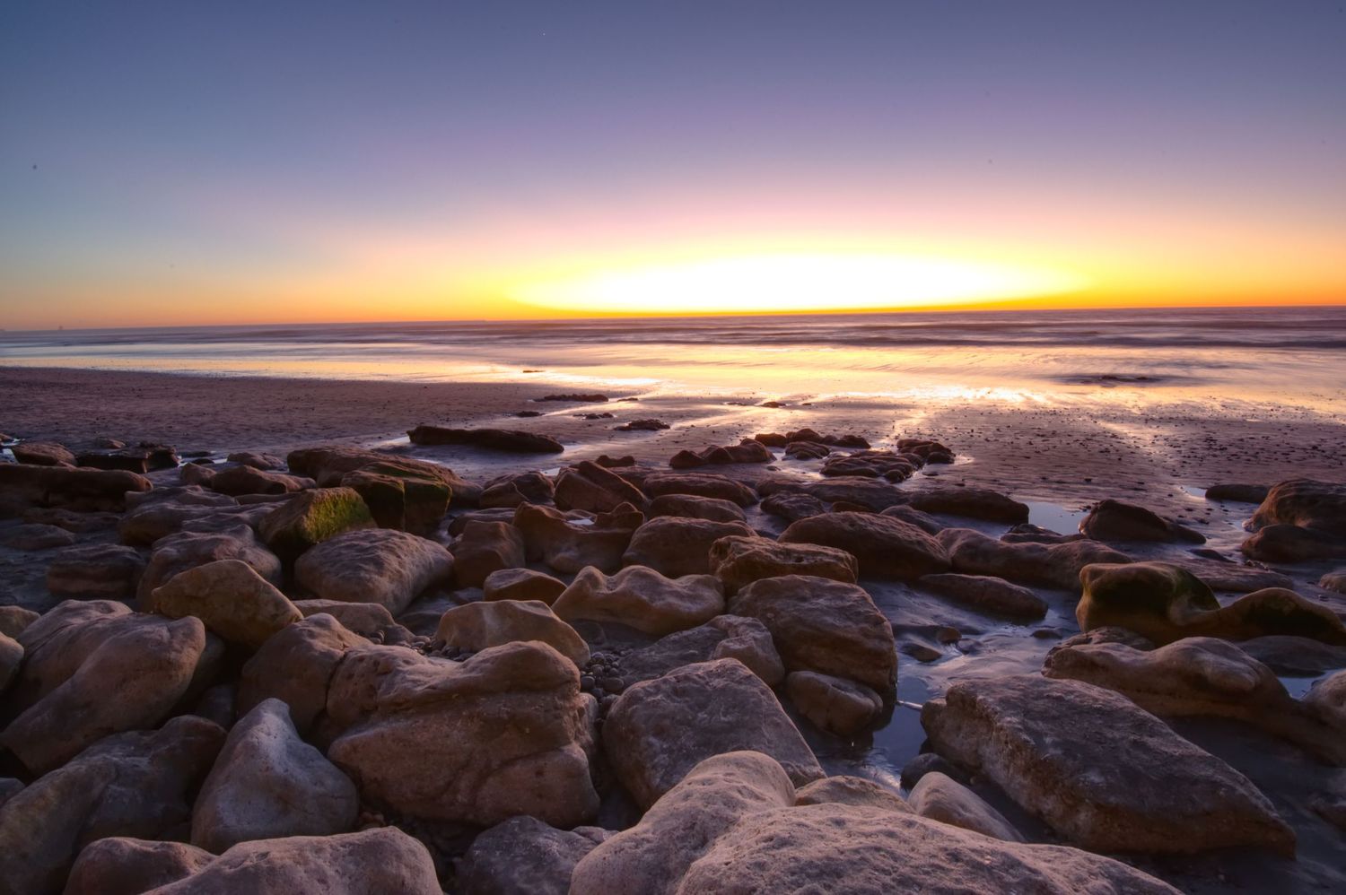 Sunset over the ocean with dramatic sky giving light to rocky beach.