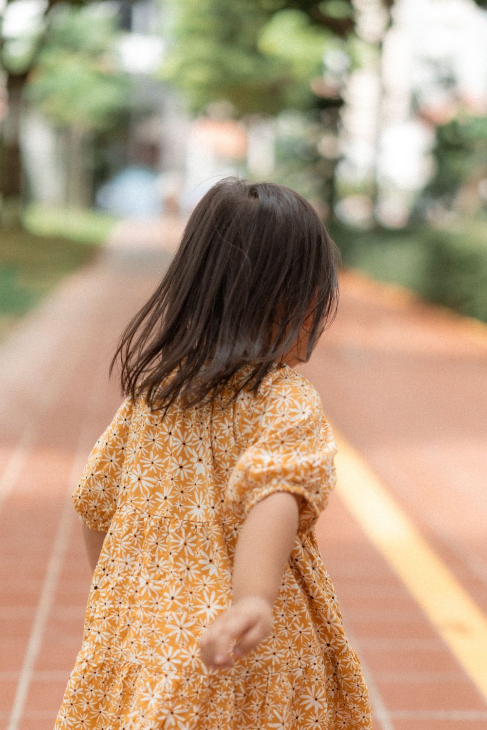 Back view of child in yellow floral dress walking on brick pathway.