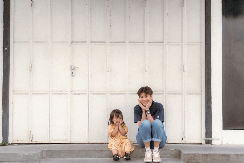 Two people sit together on white steps against a plain wall.