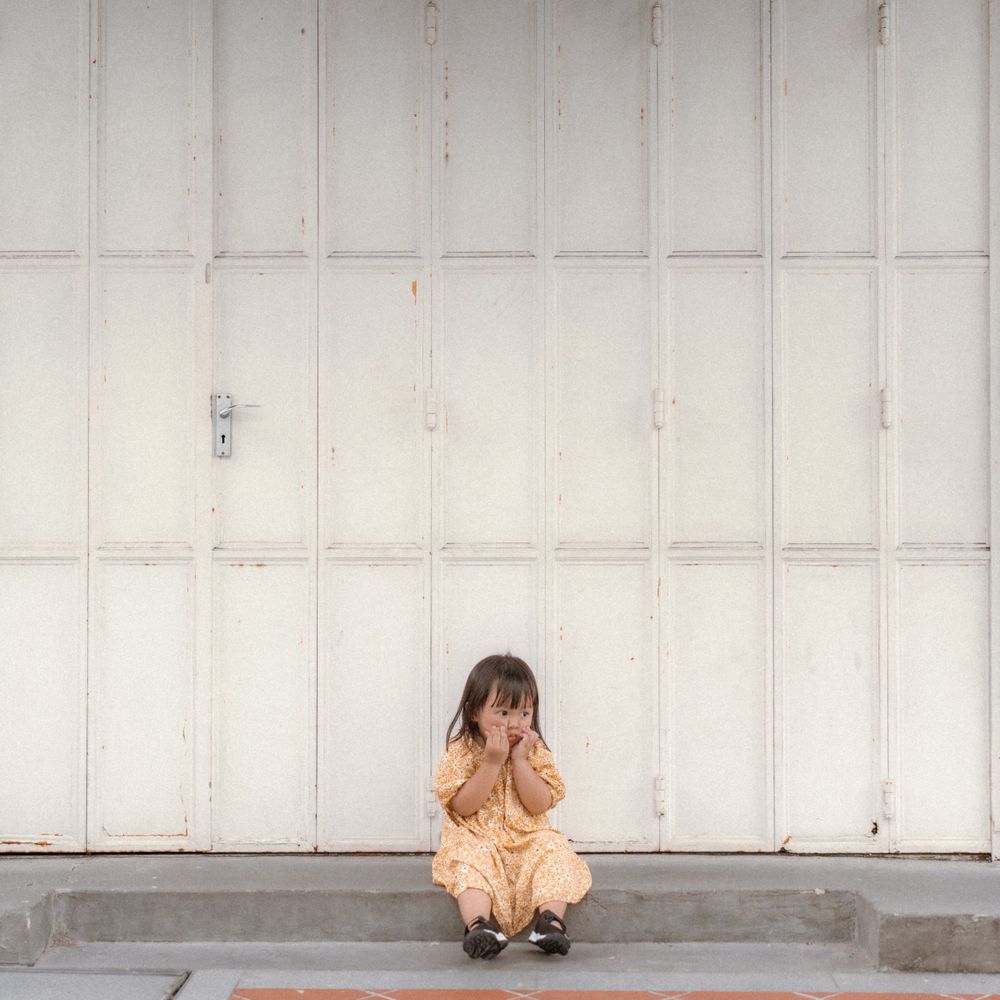 A small figure crouches against a white industrial door.