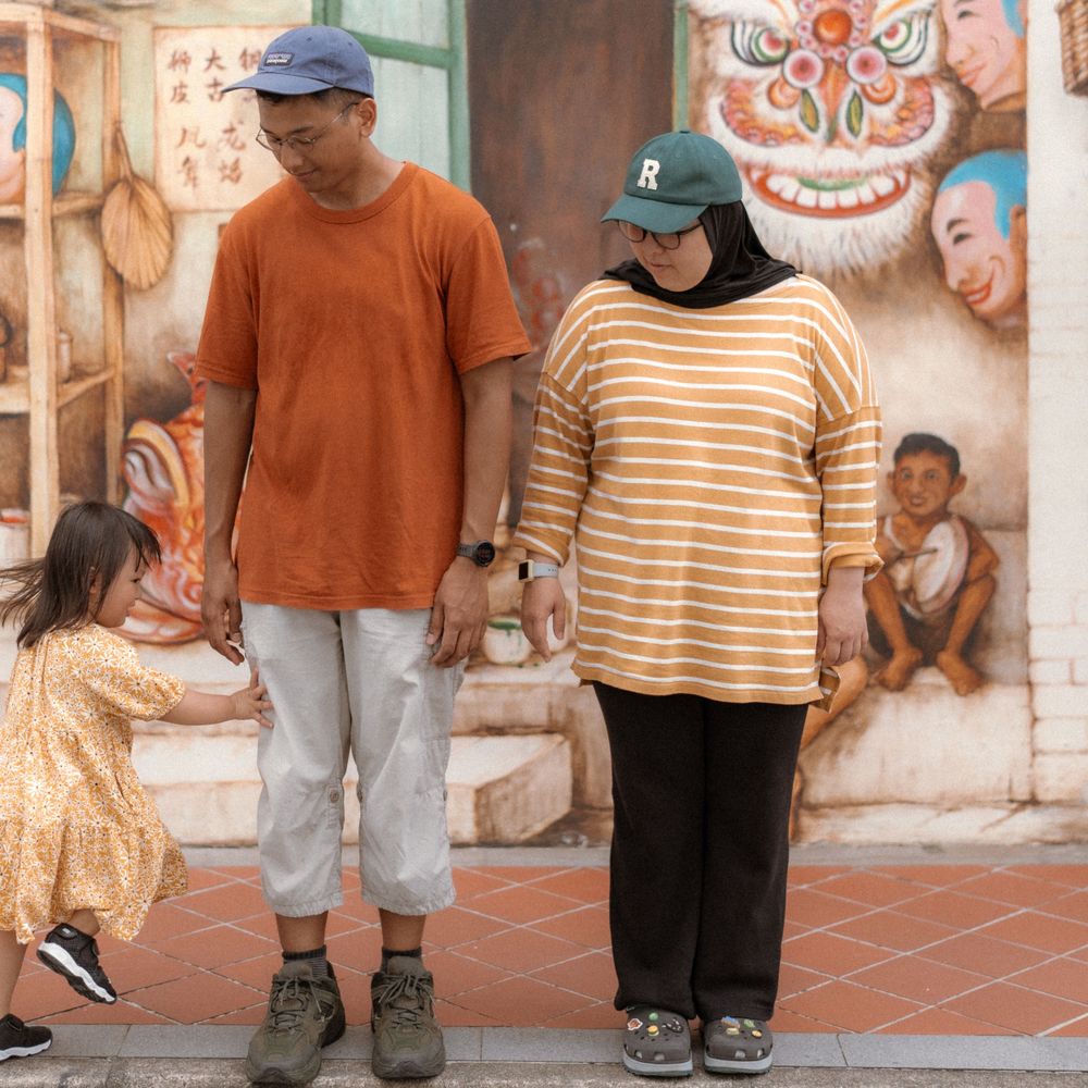 A family in casual attire stands together against a colorful mural wall with traditional designs.