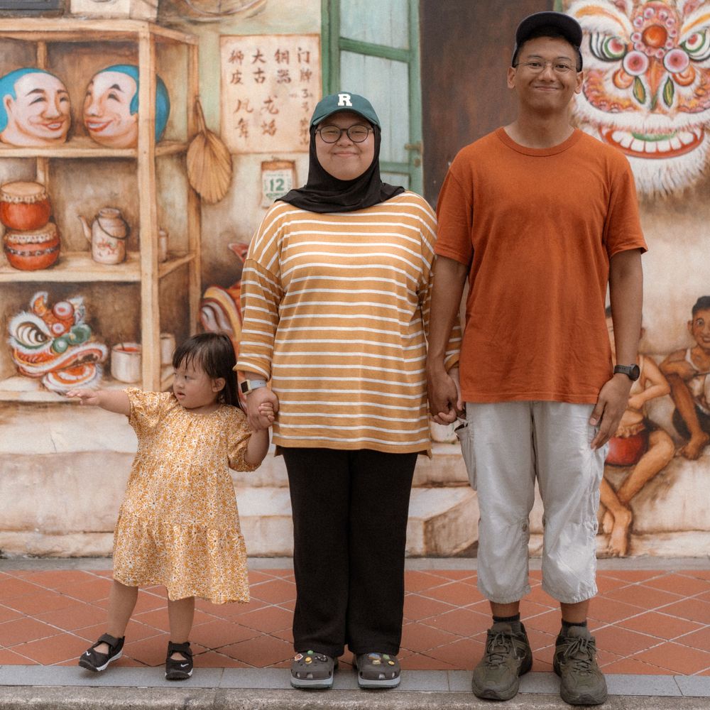 A family stands together against a wall decorated with traditional Chinese masks and art.
