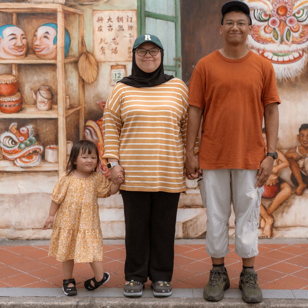 A family poses together against a decorative wall with Chinese artwork and masks.