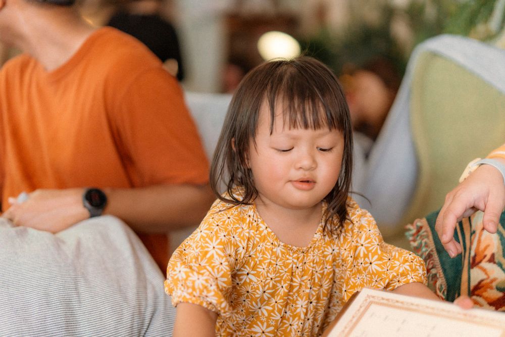 A child in an orange floral dress looks down with concentration.