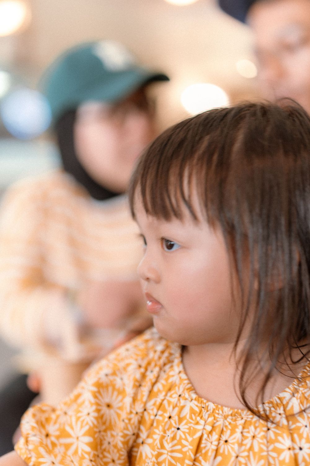 A young child in a yellow floral dress gazes thoughtfully to the side.