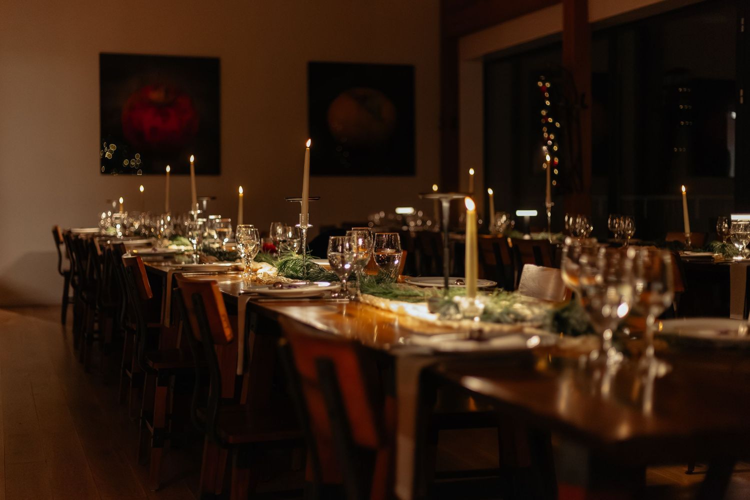 Elegant candlelit wedding reception dinner table set with glassware, greenery, and tall taper candles in a cozy venue.