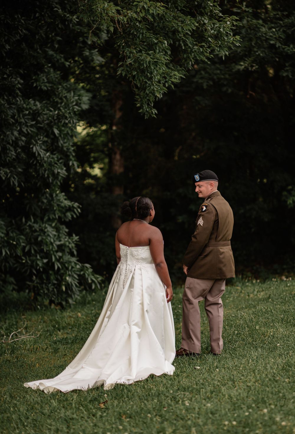 A couple shares a private moment on a grassy hillside, with the bride wearing a flowing white wedding gown.