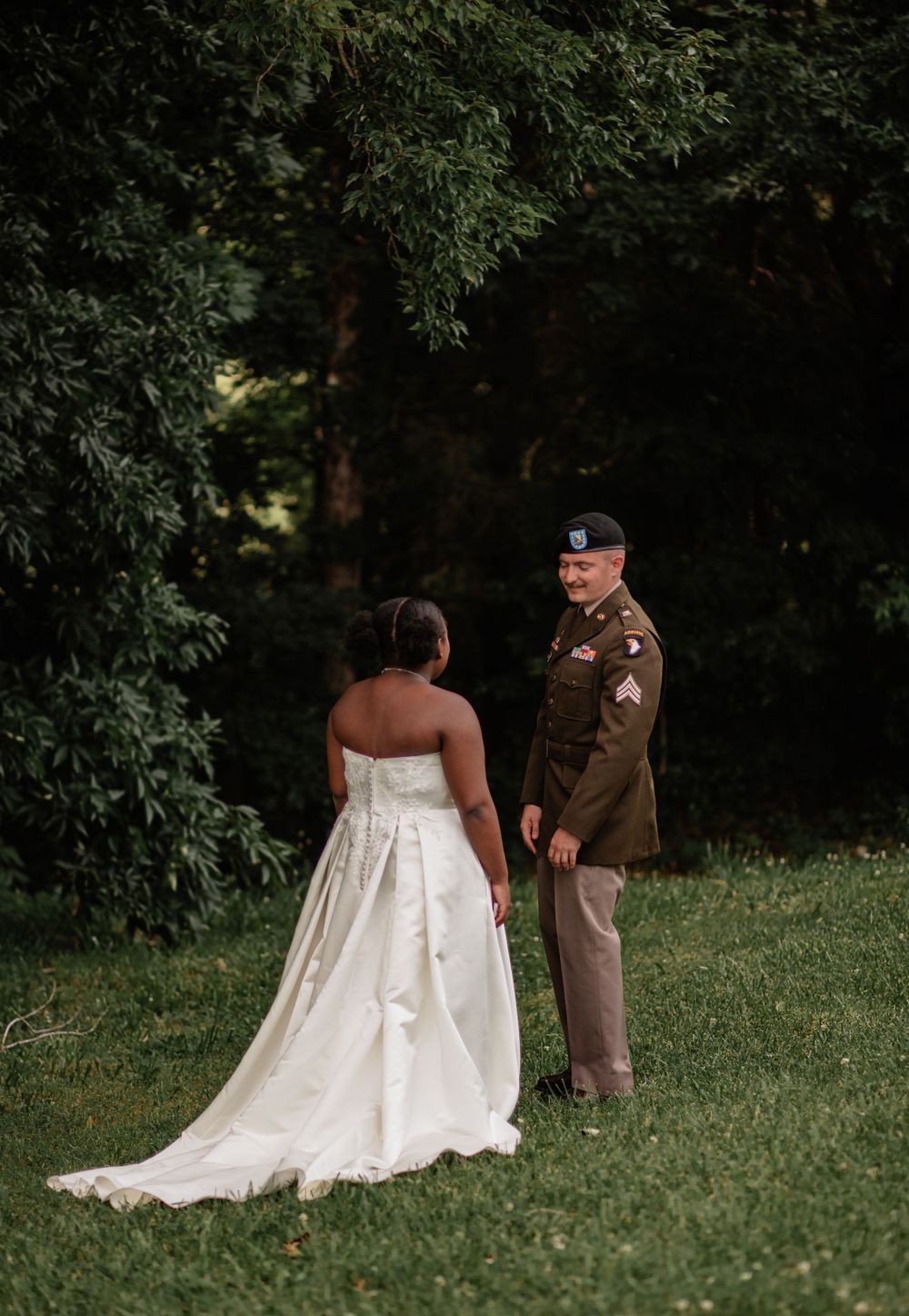 A couple walks together on a green lawn, with the bride's white dress trailing behind them.