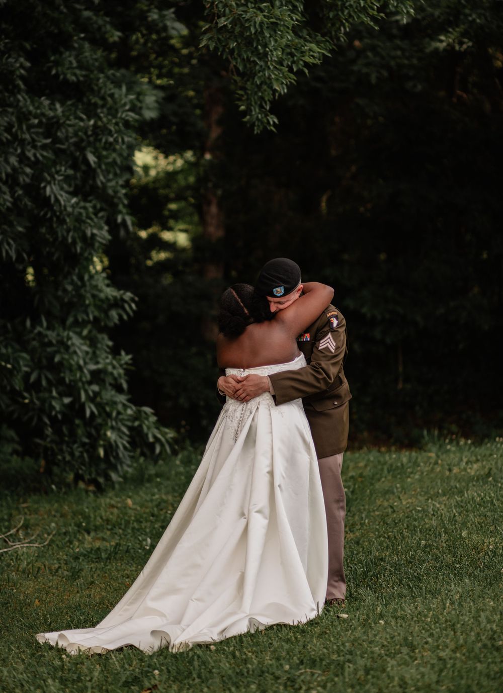 A heartfelt hug between newlyweds on a grassy hill surrounded by trees.