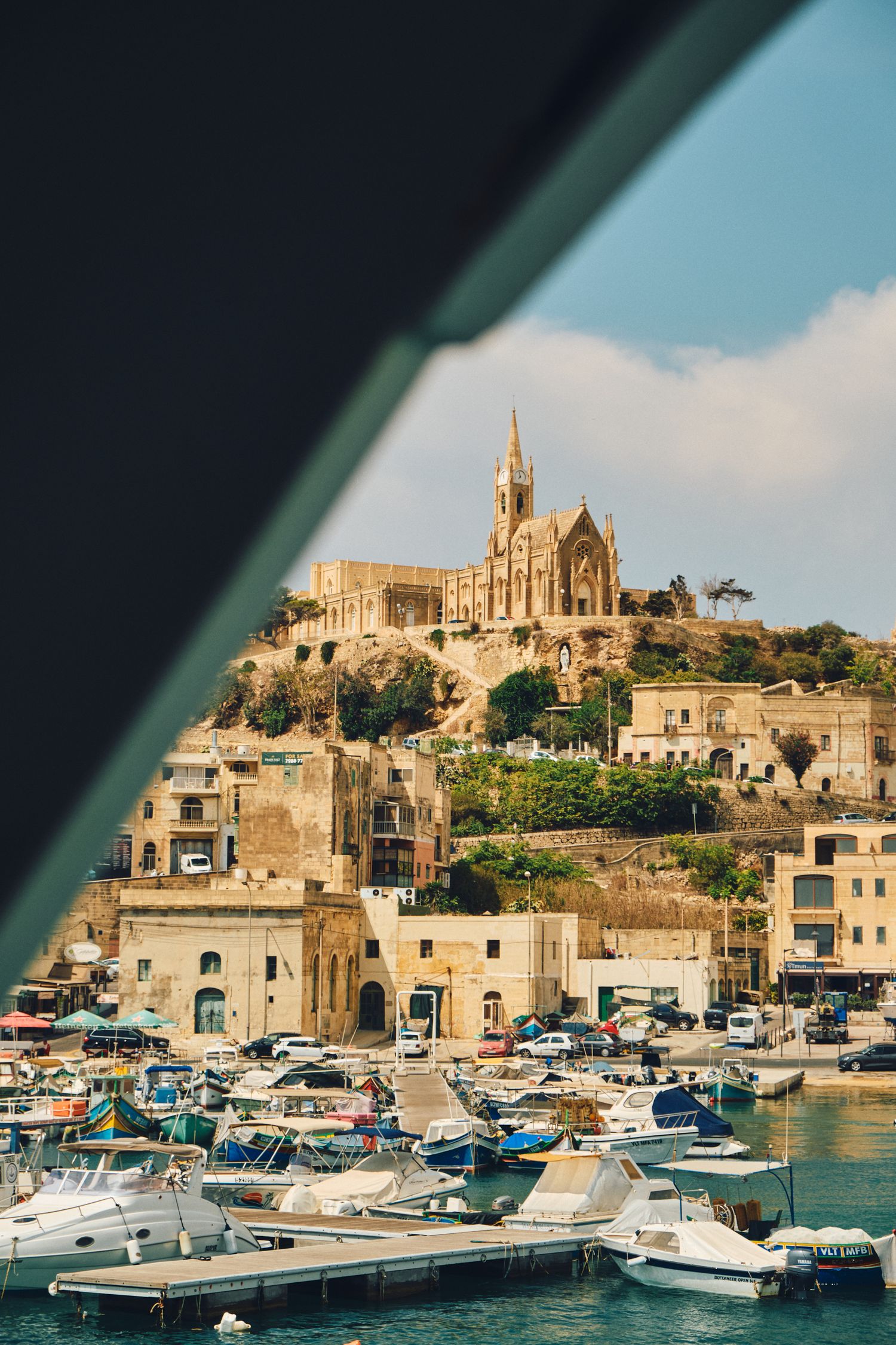 Historic church perched on a hilltop overlooking a Mediterranean harbor filled with boats in Malta.
