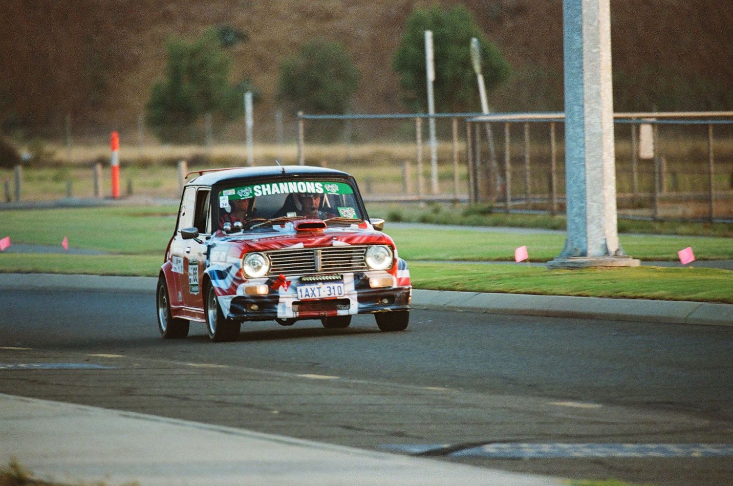 Vintage red Mini Cooper racing around a corner on a motorsport track.