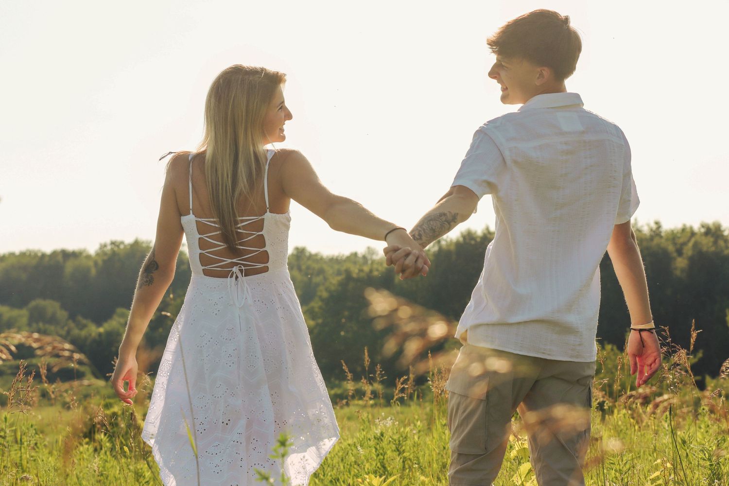 Couple holding hands while walking through a golden meadow at sunset.