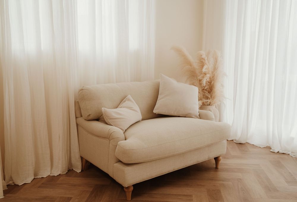 White curtains and armchairs create a bright, minimalist living space with natural sunlight filtering through sheer drapes.