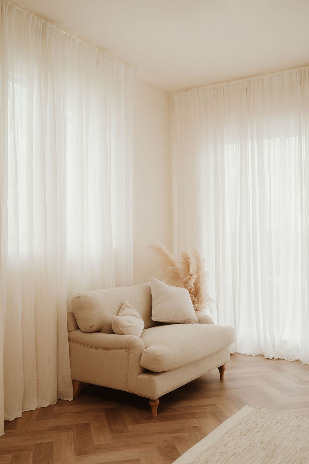 Minimalist white room with a beige loveseat against sheer curtains showcasing a clean, modern aesthetic.