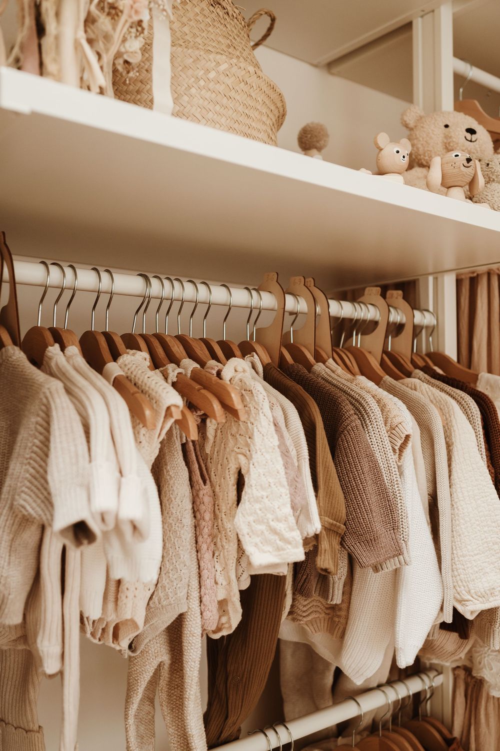 A row of neutral-colored knit baby clothes and sweaters hanging neatly on white hangers in a closet.