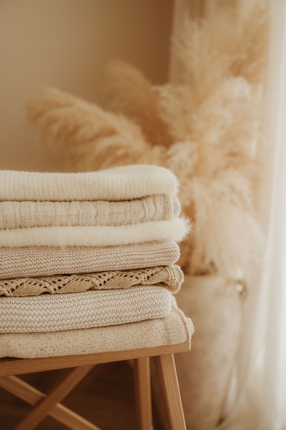 Folded beige textiles and linens stacked neatly on wooden surface in warm neutral tones.