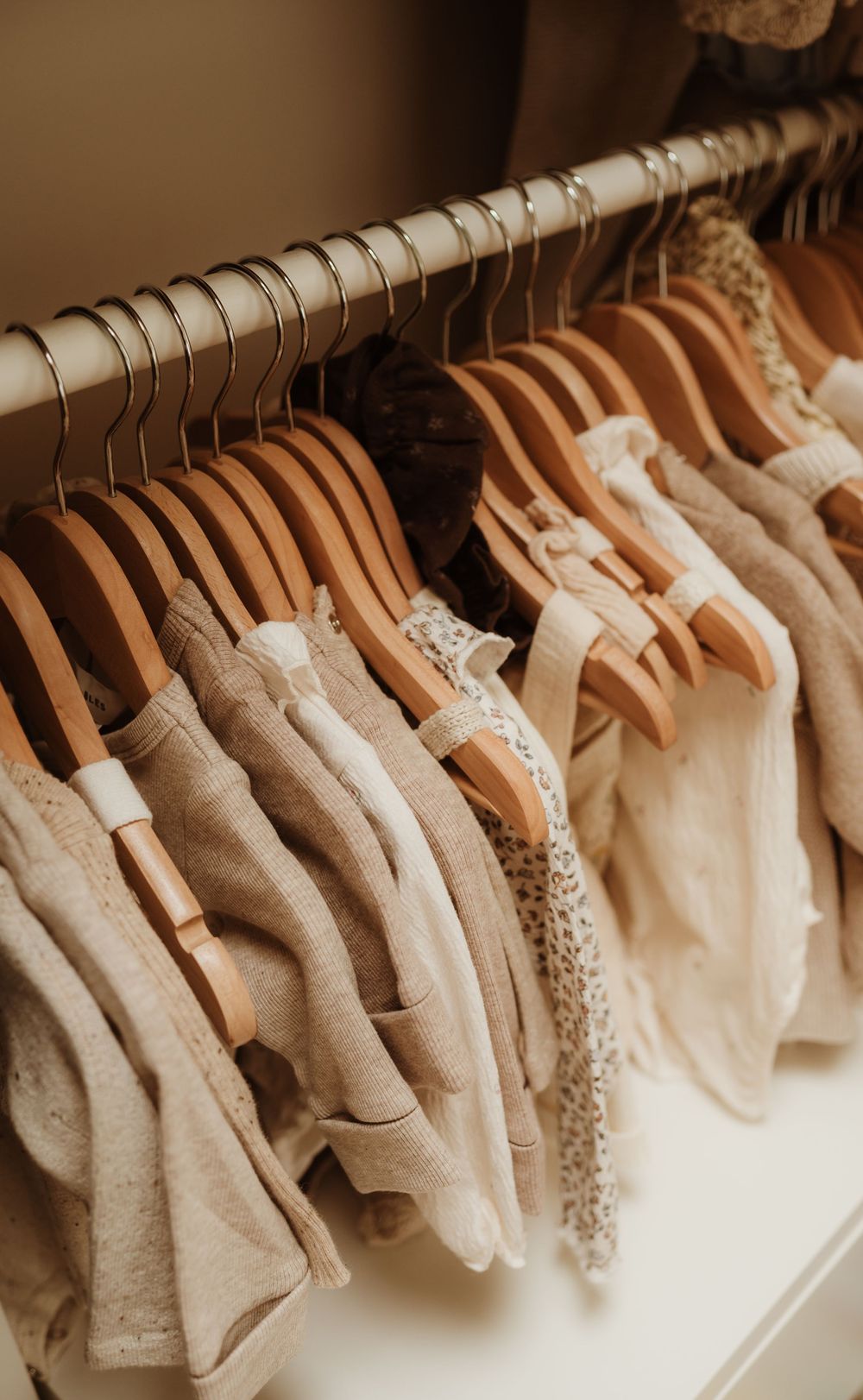 A collection of white and cream colored wedding dresses hanging on wooden hangers displayed on a rack.