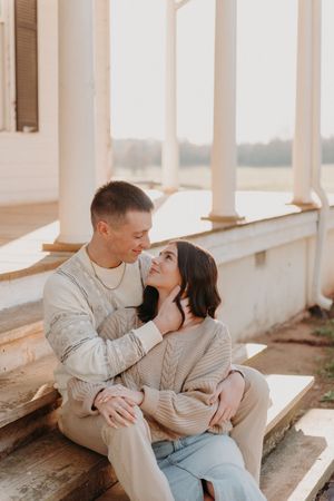 Romantic couple sharing tender moment on sunlit porch wearing matching beige sweaters.