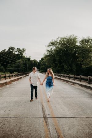 A couple holding hands while walking across a rustic bridge together.