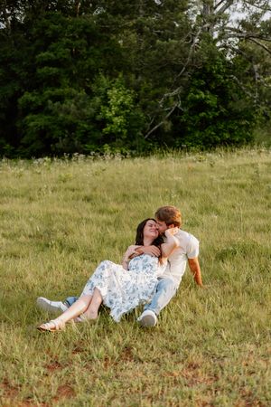 Two figures in white lie together in a sunny meadow filled with delicate red wildflowers and tall grass.