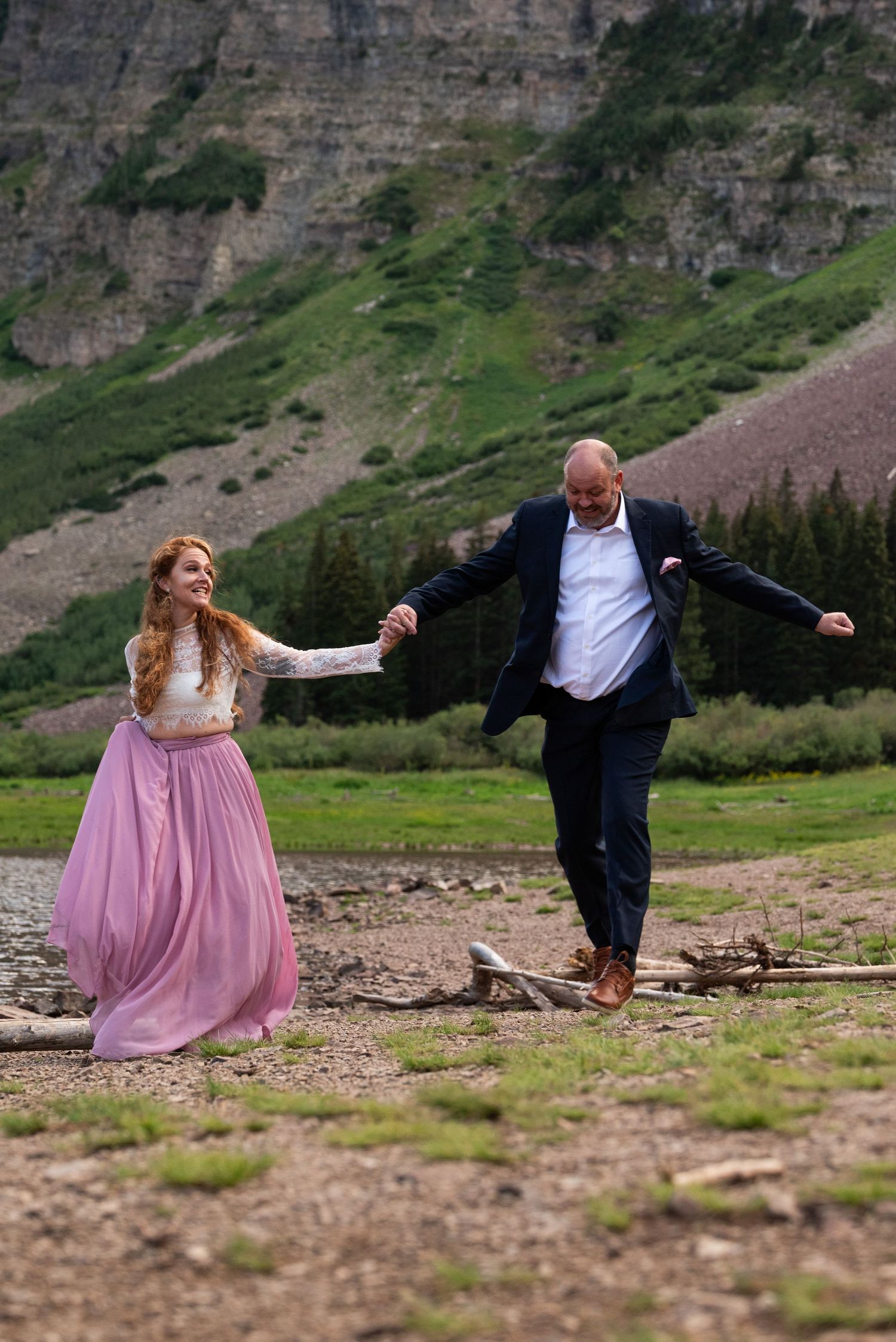 A playful moment between two people in formal wear against a backdrop of mountain cliffs.