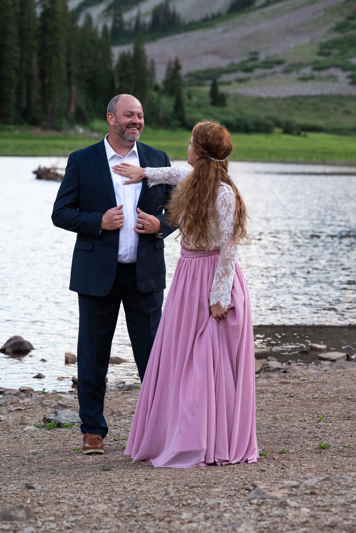 A joyful interaction between two people in formal wear by a serene mountain lake.
