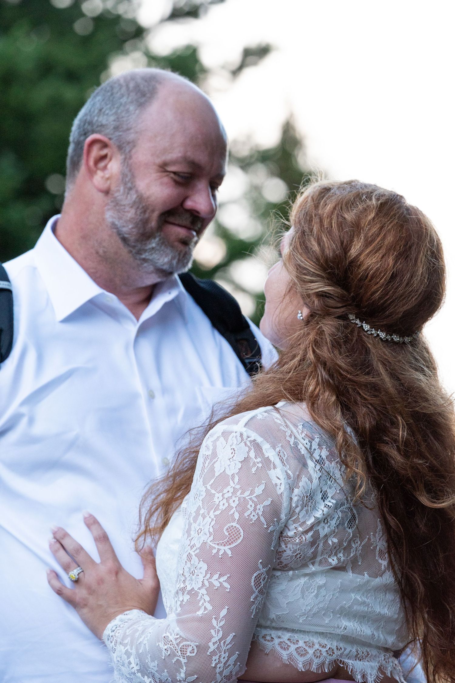 A tender moment between newlyweds wearing white and lace against a natural outdoor backdrop.