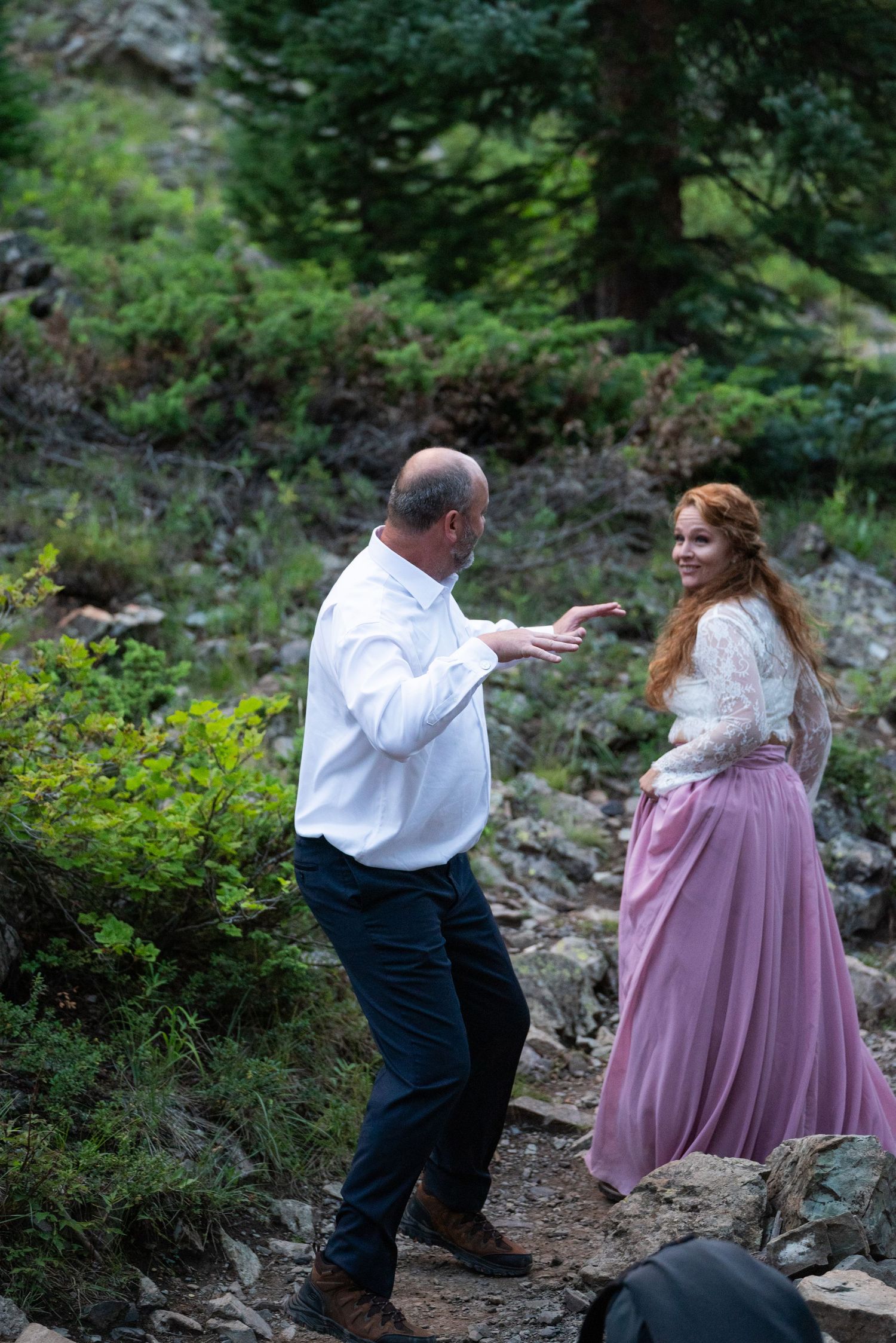 A couple shares playful moments on a rocky mountain trail surrounded by greenery.