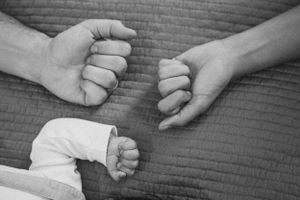 Close-up black and white image of three hands resting on textured fabric.