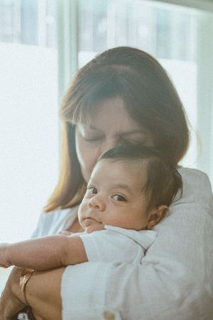 A tender embrace between parent and infant in soft natural lighting by a window.