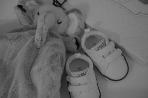 Stuffed elephant toy next to white baby sneakers in black and white.