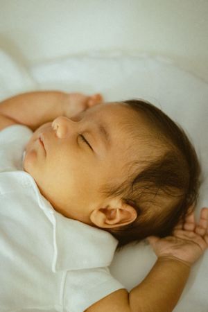 Sleeping baby in white clothing against light bedding.