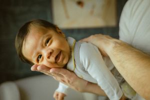 Smiling baby being held while wearing light colored clothing.