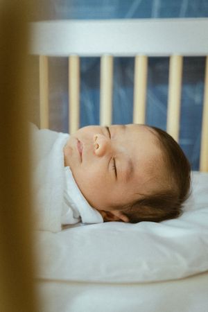 Peaceful sleeping baby photographed through crib slats.