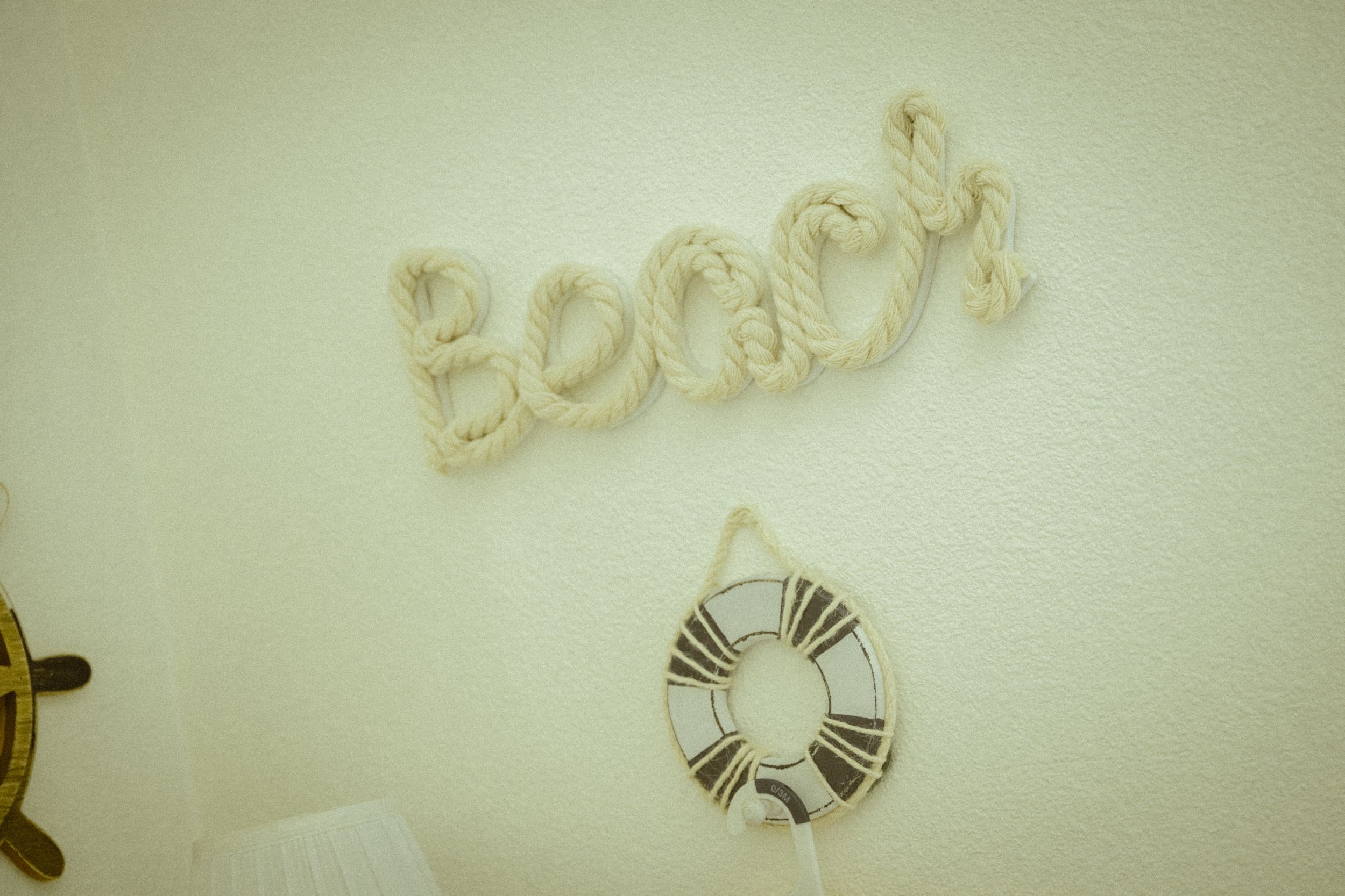 The word 'Boom' written in cursive rope letters on a white wall.