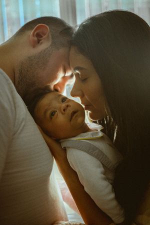 A tender family moment showing parents leaning close to their young child in warm sunlight.