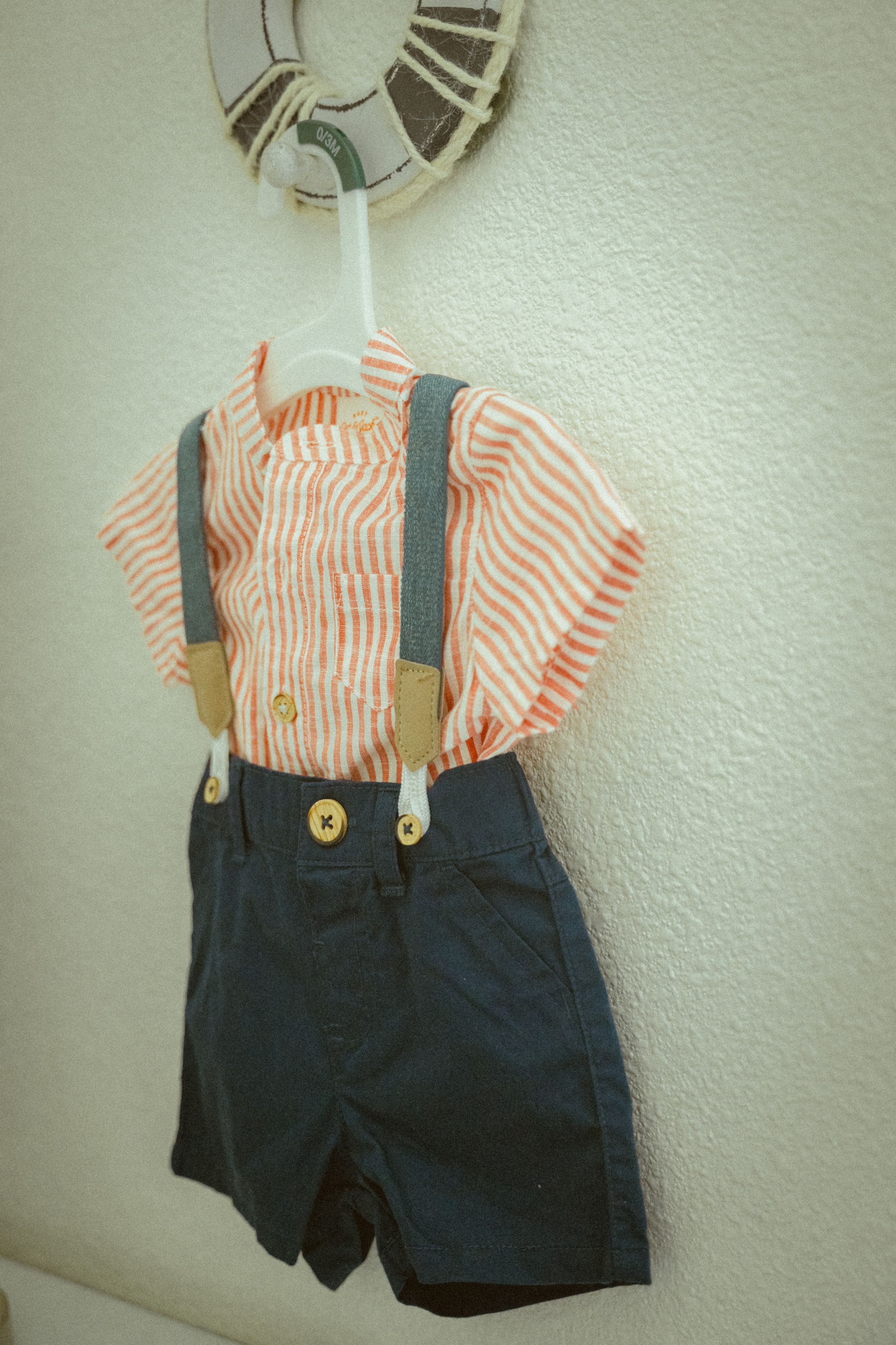 A child's outfit with navy shorts and suspenders paired with a striped shirt hanging on display.
