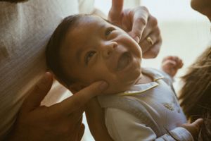 A close-up shot of a smiling baby being held by loving hands.