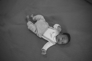 Black and white photograph of an infant laying on a textured mat.
