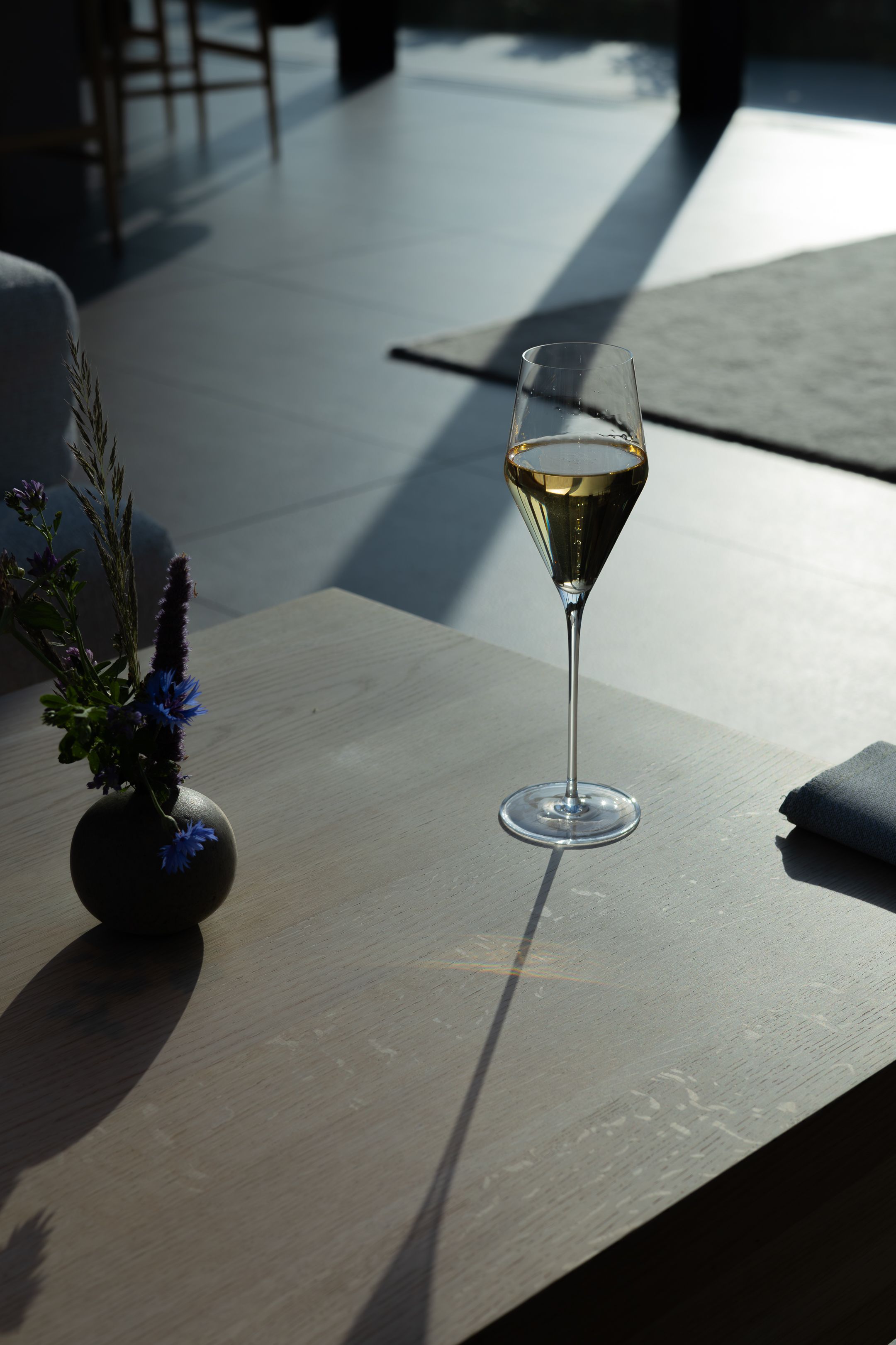Wine glass casting long shadows on minimalist table with small floral arrangement.