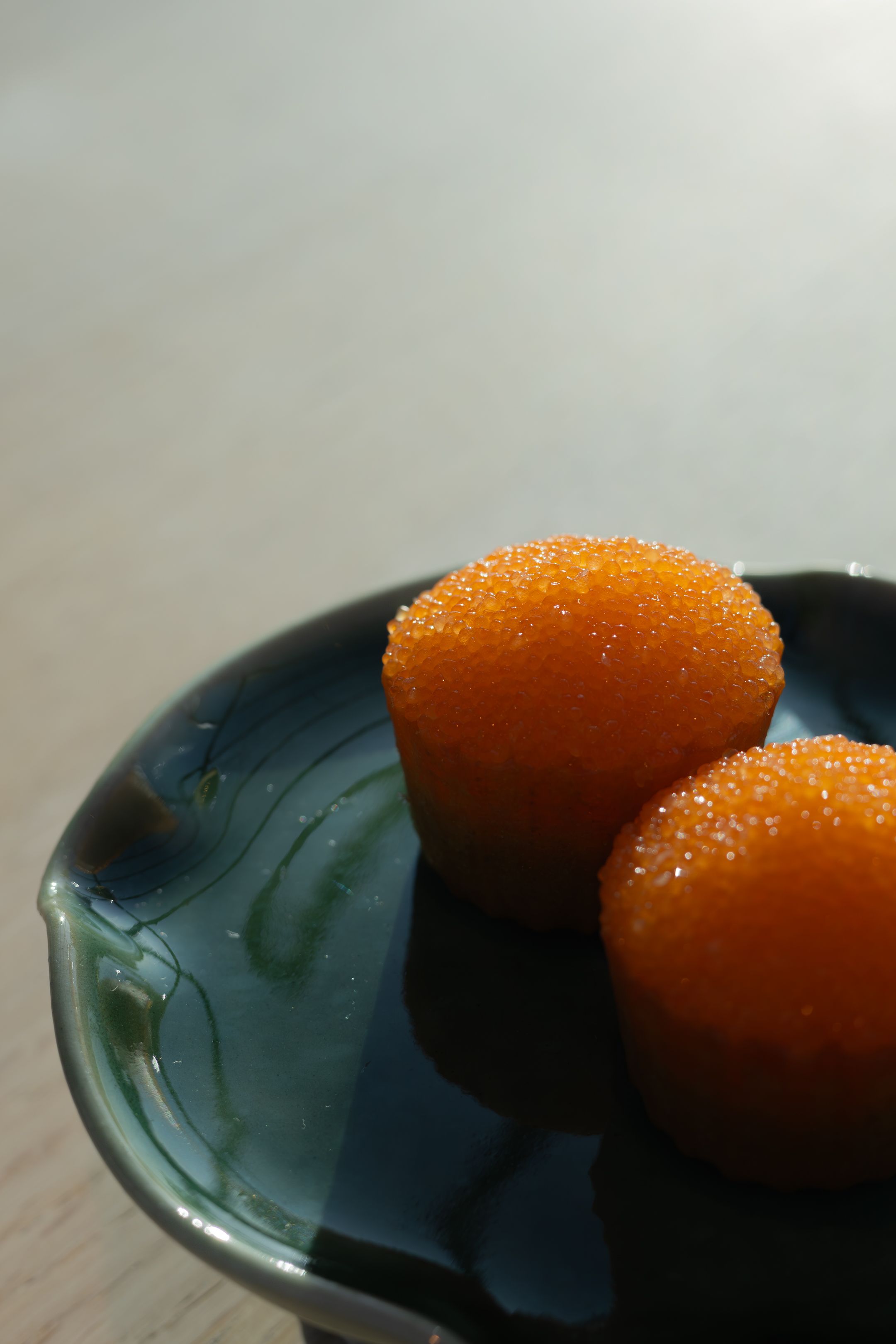 Two bright orange spherical desserts with sugary coating on dark ceramic plate.