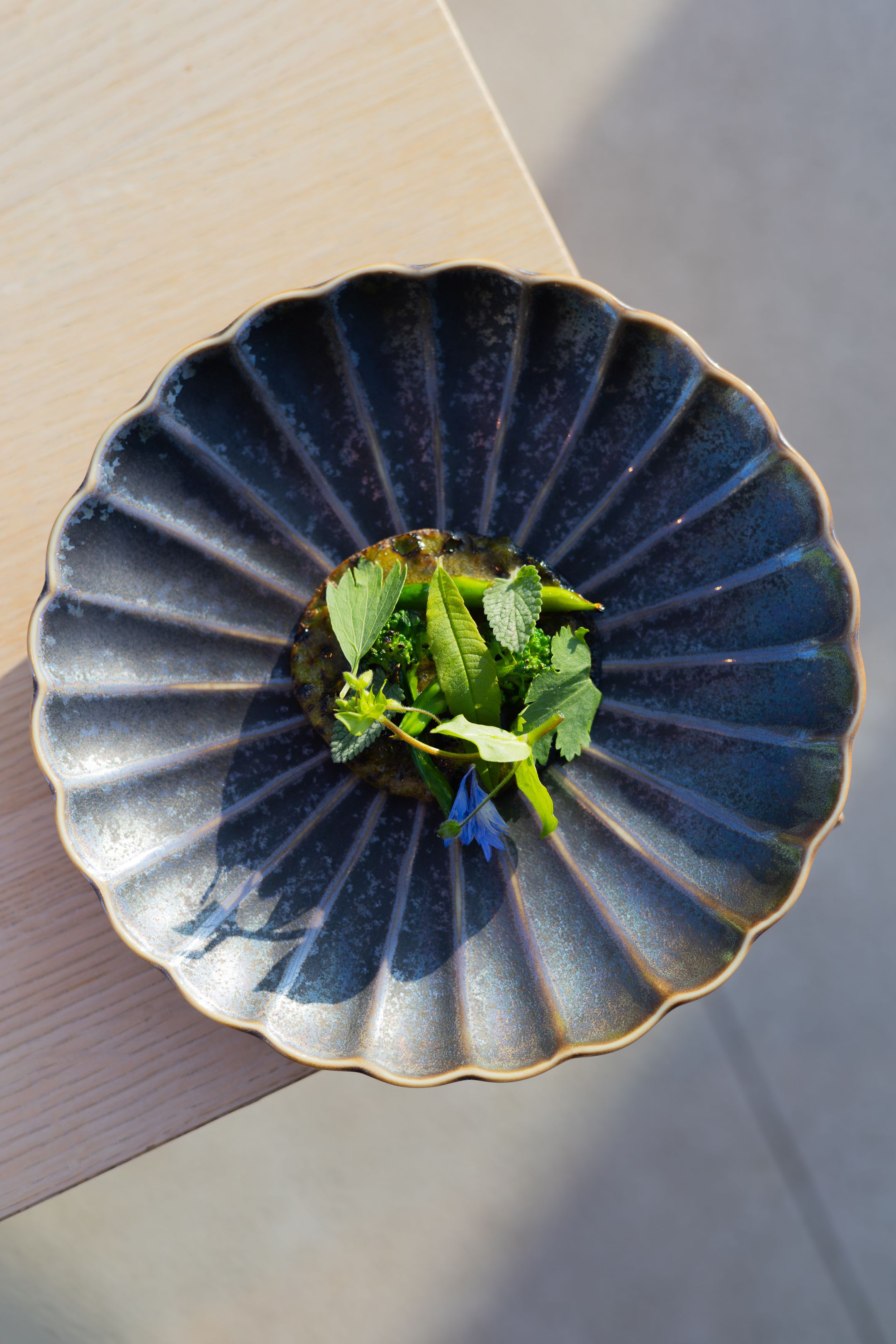 Navy blue fluted ceramic bowl containing fresh green herbs viewed from above.