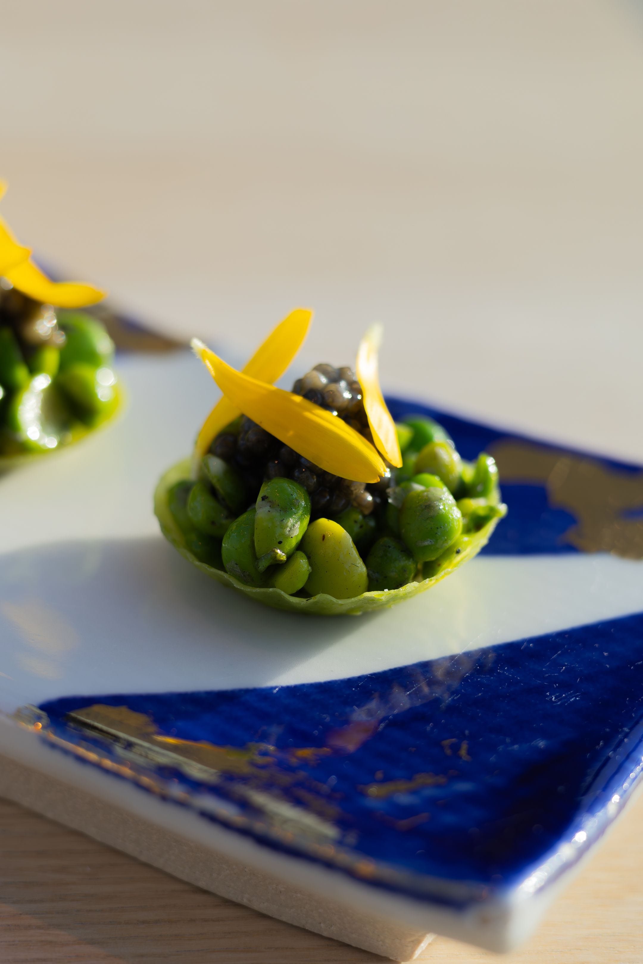 Green peas and yellow citrus garnish served in artistic blue ceramic dish.